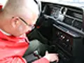 Mężczyzna w czerwonej kurtce pochyla się nad deską rozdzielczą, szukając rozwiązania, **co zrobić żeby radio nie szumiało**.