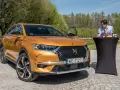 Pomarańczowy DS7 Crossback z otwartymi drzwiami, obok stolik z winem i bagietką. Nawet wady ds7 nie psują uroku tej sceny.