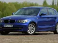 Błękitne BMW E87 z polskimi tablicami WI 3114J, z nowymi żarówkami w reflektorach, zaparkowane na bruku.