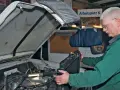 Mechanik w zielonym kombinezonie wykonuje wymianę chłodnicy krok po kroku w warsztacie.