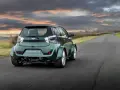 Zielony Aston Martin Cygnet V8 z szerokimi błotnikami pędzi po wiejskiej drodze pod dramatycznym, zachodzącym słońcem.