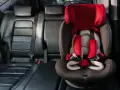 Czerwony fotelik dziecięcy z pasami bezpieczeństwa zamontowany w samochodzie. System isofix w samochodzie zapewnia bezpieczne podróżowanie najmłodszych.