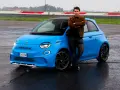 Mężczyzna opiera się o jaskrawo niebieski Abarth 500e na mokrym torze wyścigowym.