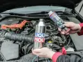 Dwie ręce trzymają produkty Liqui Moly, jeden metalowy, drugi w sprayu, gotowe do czyszczenia katalizatora w silniku samochodu.