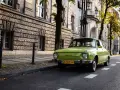 Zielony, zabytkowy samochód, prawdopodobnie 25-30 lat, zaparkowany przy kamiennej kamienicy.