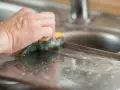 Ręka czyści zmatowiałą powierzchnię zlewu, pokazując jak wyczyścić utlenione aluminium.