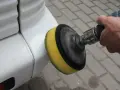 Ręka trzyma polerkę z żółtą gąbką, która poleruje biały zderzak. Dowiedz się, jak wypolerować samochód.