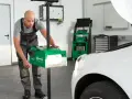 Mechanik dokonuje ręcznej regulacji świateł samochodu za pomocą zielonego urządzenia.