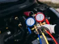 Profesjonalny serwis klimatyzacji samochodowej. Mechanik z manometrami sprawdza układ chłodzenia silnika.