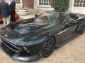 Elegancki, czarny Aston Martin Victor błyszczy na tle ceglanego budynku. Jego aerodynamiczna linia i unikalne felgi przyciągają wzrok.