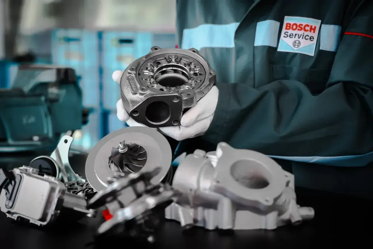 Mechanik w fartuchu Bosch Service prezentuje części turbosprężarki. Dowiedz się, jak jeździć dieslem, by cieszyć się jego mocą.