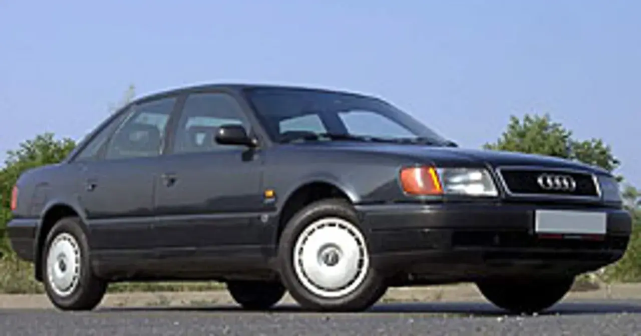 Klasyczny, ciemnoszary Audi A6 C4 z lat 90. stoi na tle błękitnego nieba i zieleni.