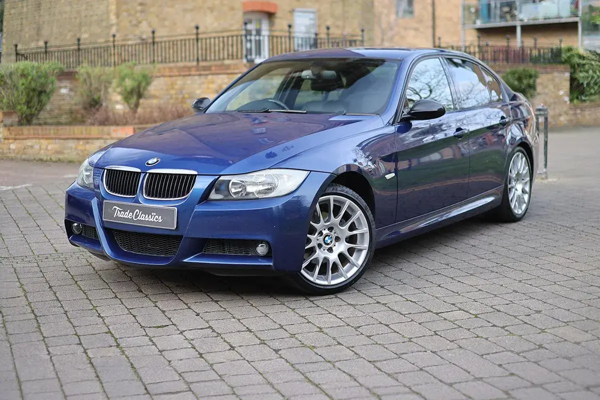 Błękitne BMW 320si z felgami M-pakietu stoi na brukowanym podjeździe.