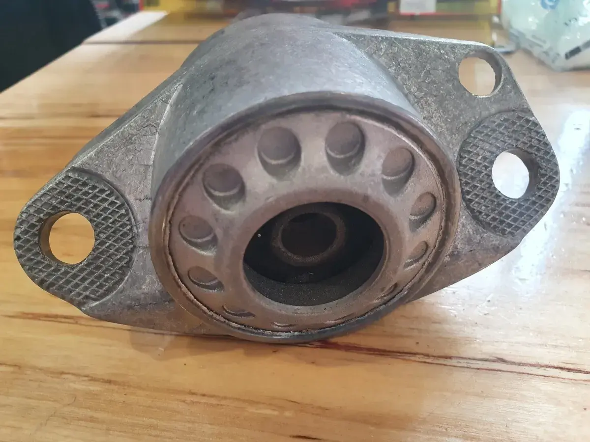 Metalowy element zawieszenia auta, przypominający kielichy, leży na drewnianym blacie.