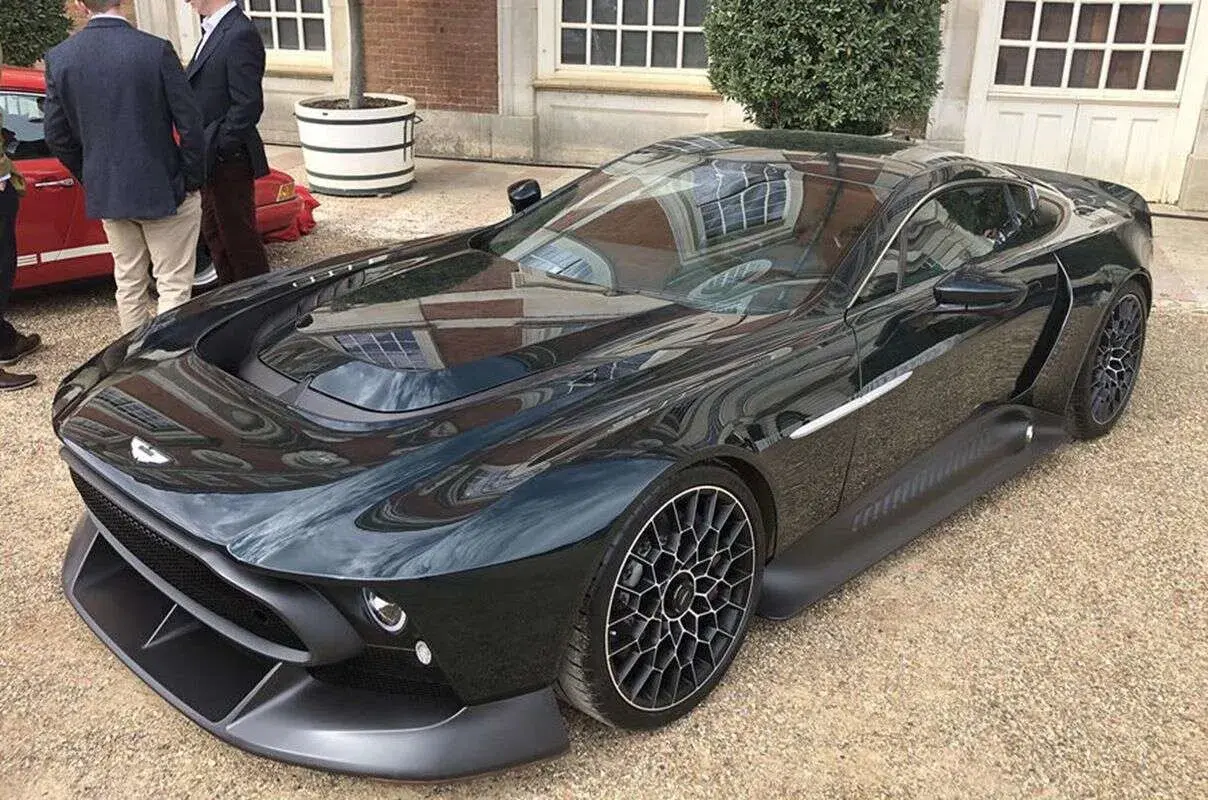 Elegancki, czarny Aston Martin Victor błyszczy na tle ceglanego budynku. Jego aerodynamiczna linia i unikalne felgi przyciągają wzrok.