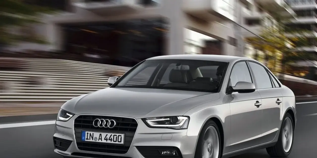 Srebrne Audi A4 B8 w ruchu miejskim, znane z typowych usterek, pędzi ulicą.
