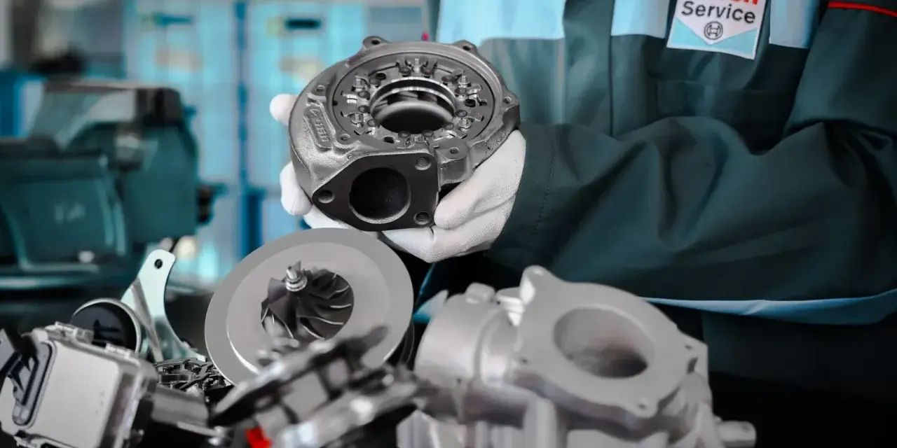 Mechanik w fartuchu Bosch Service prezentuje części turbosprężarki. Dowiedz się, jak jeździć dieslem, by cieszyć się jego mocą.