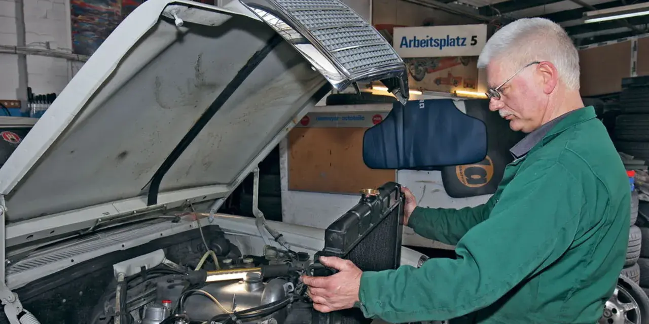 Mechanik w zielonym kombinezonie wykonuje wymianę chłodnicy krok po kroku w warsztacie.