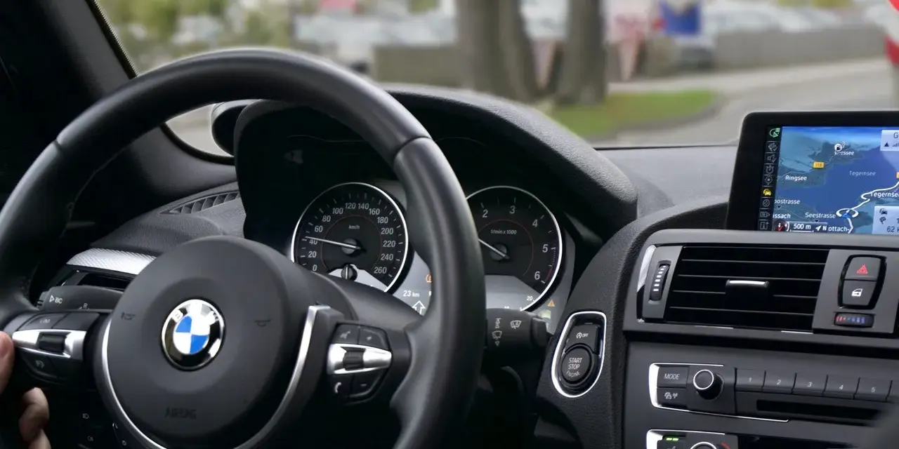 Wnętrze BMW z kierownicą i nawigacją. Kierowca sprawdza plan serwisowy przed podróżą.