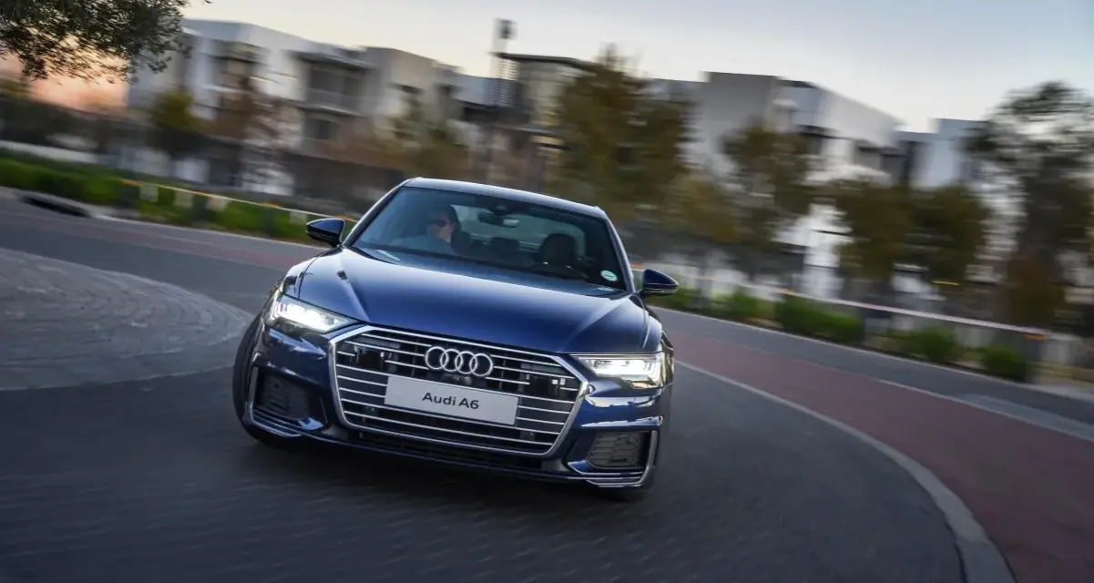 Niebieskie Audi A6 C8 w ruchu, z rozmazanym tłem budynków i drzew. Nawet przy potencjalnych usterkach, wygląda imponująco.