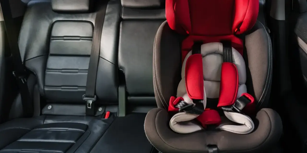Czerwony fotelik dziecięcy z pasami bezpieczeństwa zamontowany w samochodzie. System isofix w samochodzie zapewnia bezpieczne podróżowanie najmłodszych.