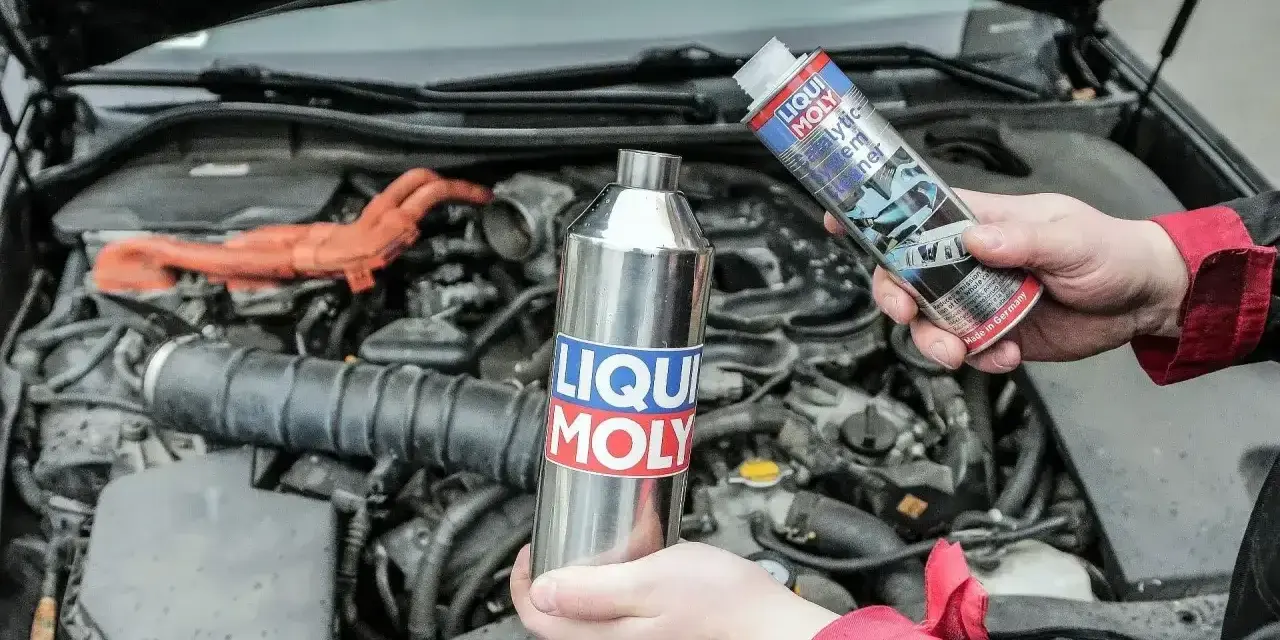 Dwie ręce trzymają produkty Liqui Moly, jeden metalowy, drugi w sprayu, gotowe do czyszczenia katalizatora w silniku samochodu.