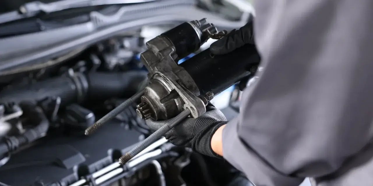 Mechanik w rękawiczkach trzyma rozrusznik na krótko, gotowy do montażu w silniku samochodu.