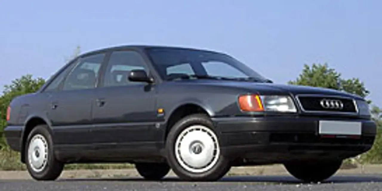 Klasyczny, ciemnoszary Audi A6 C4 z lat 90. stoi na tle błękitnego nieba i zieleni.