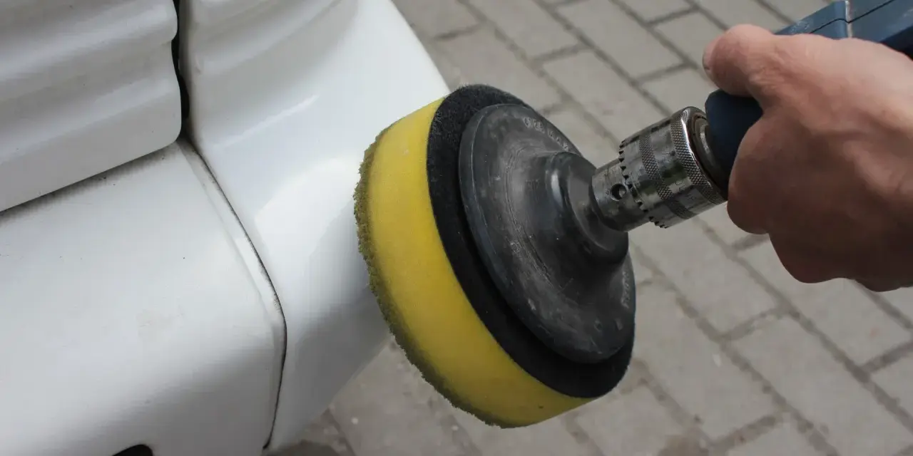 Ręka trzyma polerkę z żółtą gąbką, która poleruje biały zderzak. Dowiedz się, jak wypolerować samochód.