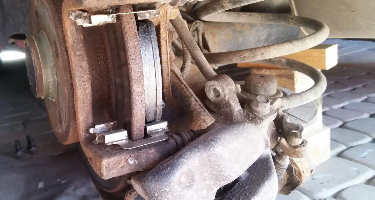 Wymiana klocków hamulcowych Opel Astra H tył. Widoczny skorodowany zacisk i tarcza hamulcowa, gotowe do montażu nowych klocków.