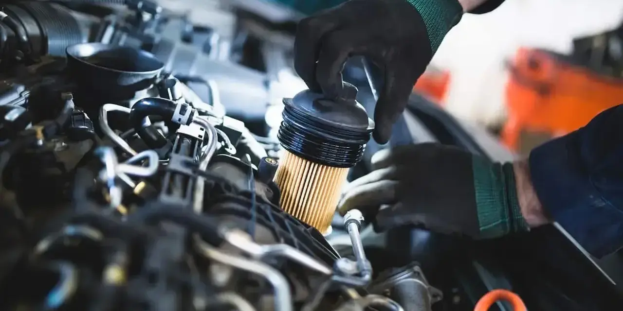 Mechanik w czarnych rękawiczkach dokonuje wymiany filtra paliwa w silniku samochodowym.
