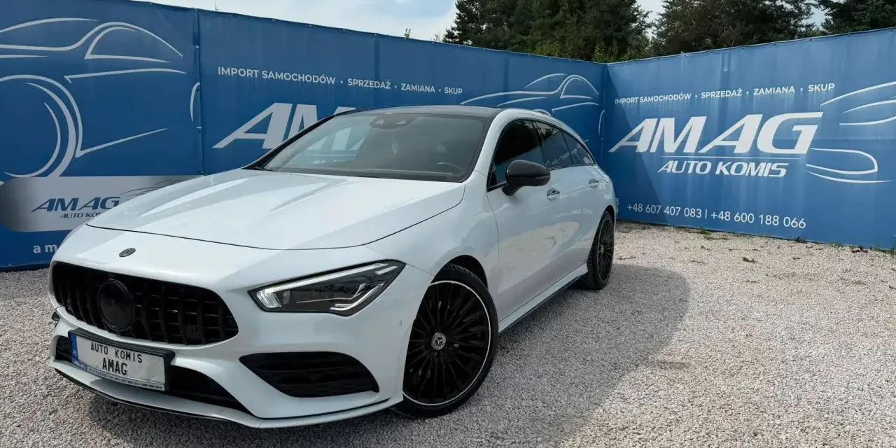 Biały Mercedes na tle niebieskiego banera AMAG Auto Komis. Idealny do akcje serwisowe Mercedes.