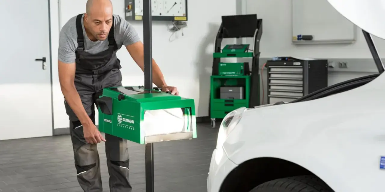 Mechanik dokonuje ręcznej regulacji świateł samochodu za pomocą zielonego urządzenia.