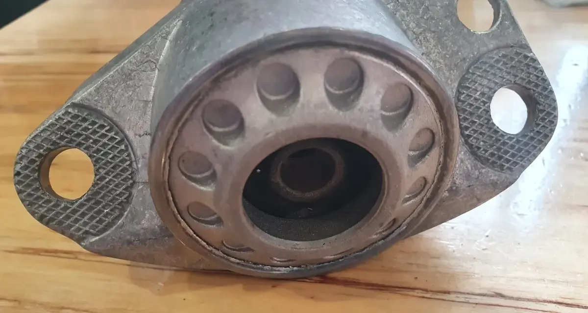 Metalowy element zawieszenia auta, przypominający kielichy, leży na drewnianym blacie.