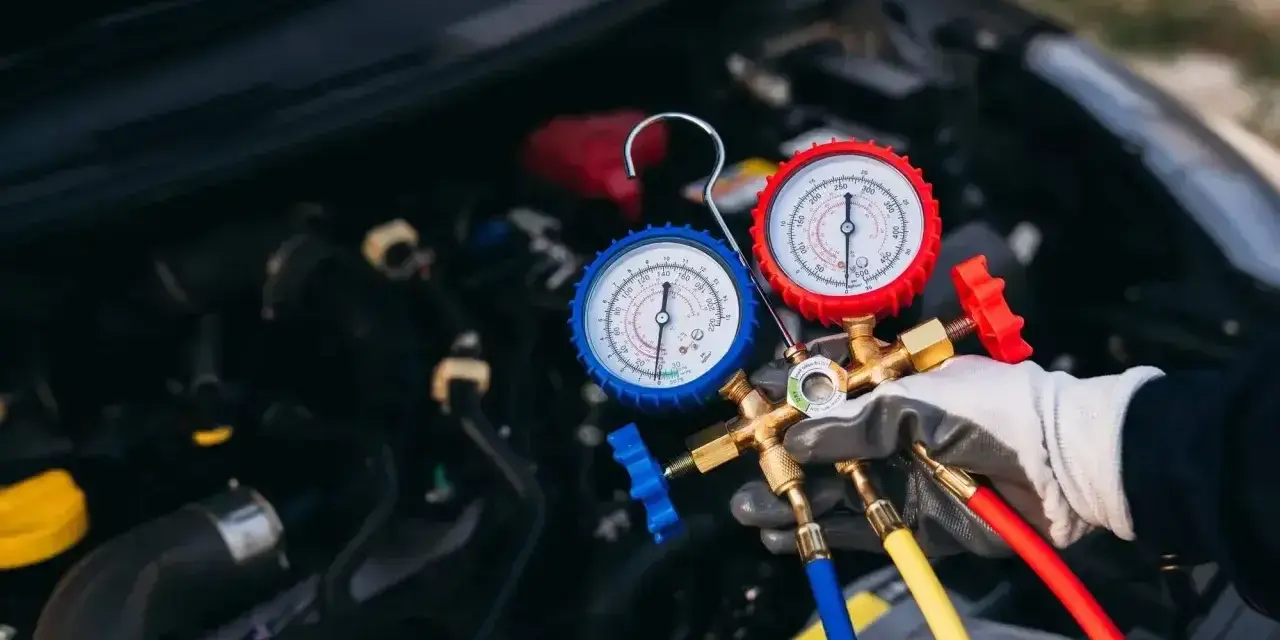 Profesjonalny serwis klimatyzacji samochodowej. Mechanik z manometrami sprawdza układ chłodzenia silnika.