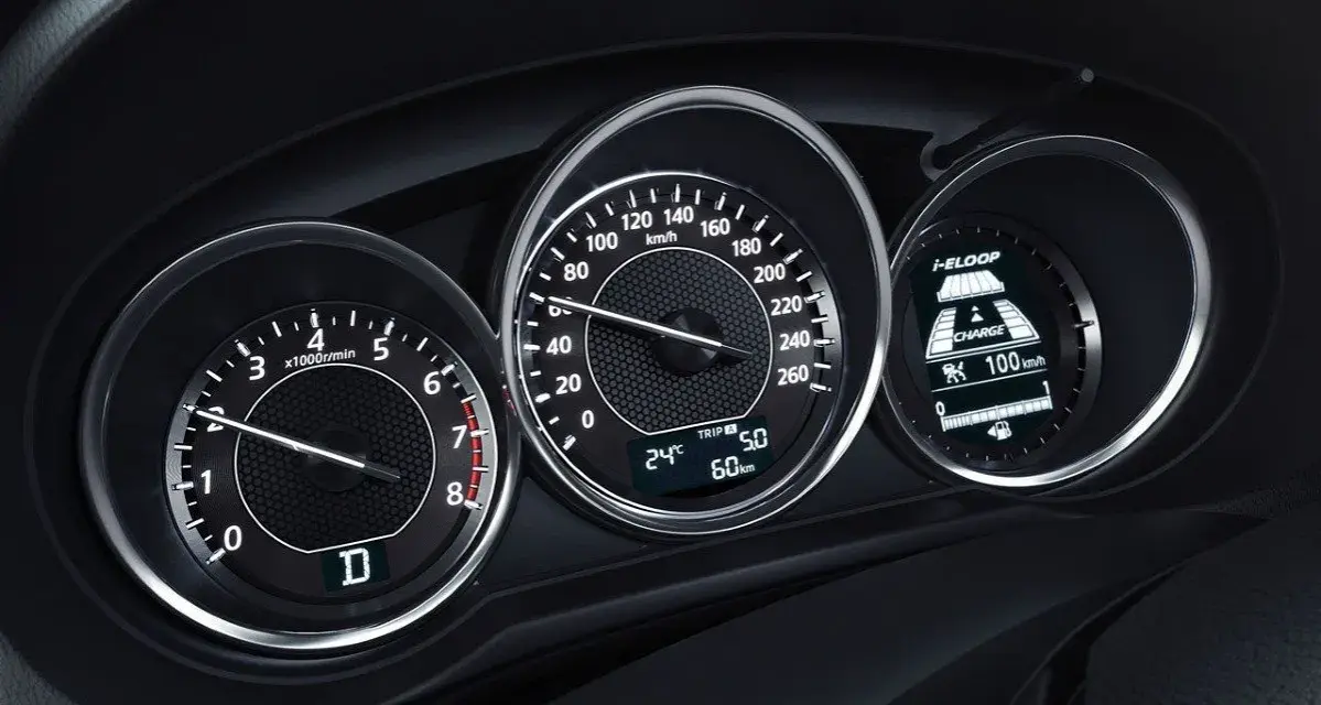 Zbliżenie na deskę rozdzielczą samochodu: obrotomierz pokazuje ok. 1500 obr./min, prędkościomierz ok. 60 km/h, a wyświetlacz i-ELOOP informuje o ładowaniu.