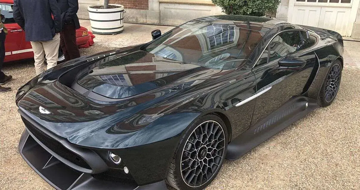 Elegancki, czarny Aston Martin Victor błyszczy na tle ceglanego budynku. Jego aerodynamiczna linia i unikalne felgi przyciągają wzrok.