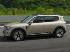 Nowoczesny, beżowy suv elektryczny pędzi po drodze, otoczony zielenią.