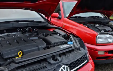 Dwa czerwone Volkswageny z otwartymi maskami. Nowszy model z silnikiem TDI obok starszego, gdzie widać stary diesel.