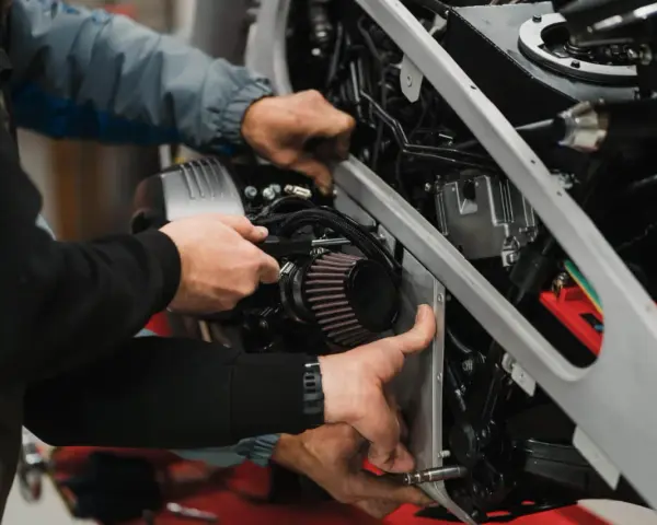 Mechanicy pracują nad motocyklem, być może rozwiązując problem zapchanego filtra paliwa powodującego szarpanie.