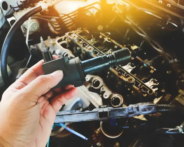 Dłoń trzyma moduł zapłonowy nad silnikiem. Dowiedz się, jak sprawdzić moduł zapłonowy, aby zapewnić prawidłowe działanie samochodu.