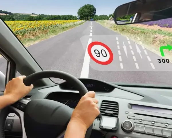 Widok z kabiny samochodu z wyświetlaczem typu head-up pokazującym ograniczenie prędkości 90 i wskazówkę skrętu w prawo za 300 m.