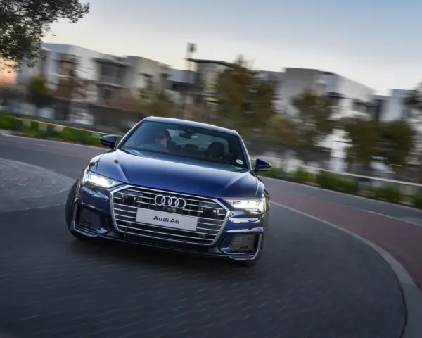 Niebieskie Audi A6 C8 w ruchu, z rozmazanym tłem budynków i drzew. Nawet przy potencjalnych usterkach, wygląda imponująco.