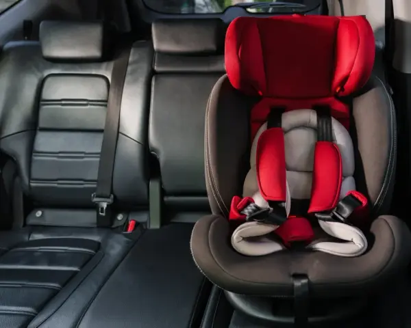 Czerwony fotelik dziecięcy z pasami bezpieczeństwa zamontowany w samochodzie. System isofix w samochodzie zapewnia bezpieczne podróżowanie najmłodszych.