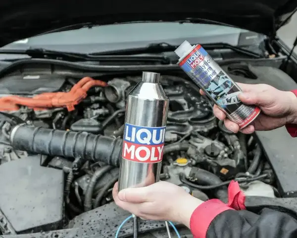 Dwie ręce trzymają produkty Liqui Moly, jeden metalowy, drugi w sprayu, gotowe do czyszczenia katalizatora w silniku samochodu.