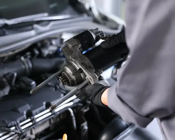 Mechanik w rękawiczkach trzyma rozrusznik na krótko, gotowy do montażu w silniku samochodu.