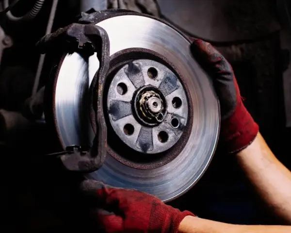 Mechanik w czerwonych rękawicach wymienia tarczę hamulcową. Upewnia się, że hamulce blokują po rozgrzaniu, by zapewnić bezpieczeństwo.