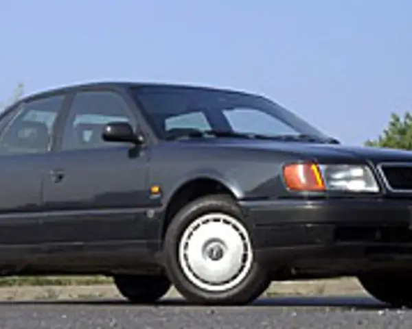 Klasyczny, ciemnoszary Audi A6 C4 z lat 90. stoi na tle błękitnego nieba i zieleni.