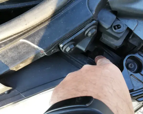 Palec wskazuje śrubę mocującą reflektor podczas wymiany żarówki audi a4 b7 przód prawa.