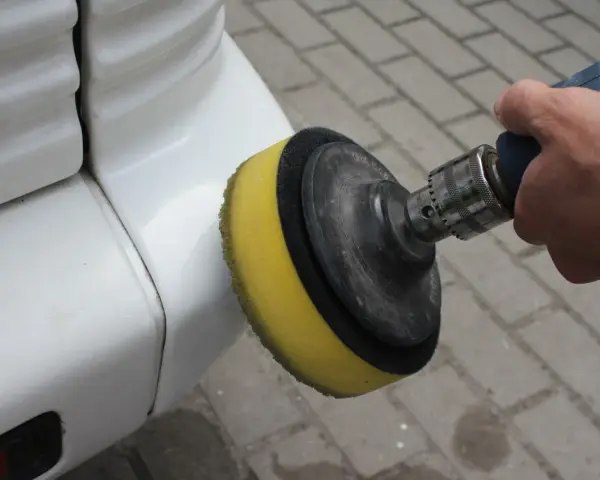Ręka trzyma polerkę z żółtą gąbką, która poleruje biały zderzak. Dowiedz się, jak wypolerować samochód.